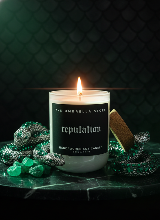 Candle labeled 'reputation' from 'The Umbrella Store' on a dark surface with decorative elements.