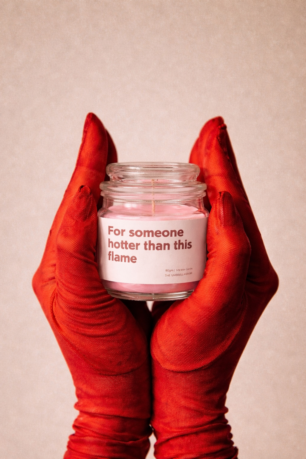 Candle in red gloves with a pink candle inside, on a beige background