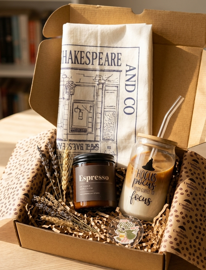 Gift box with 'Espresso' candle, 'Hocus Pocus' jar, and 'Shakespeare and Co.' bag on a wooden surface.